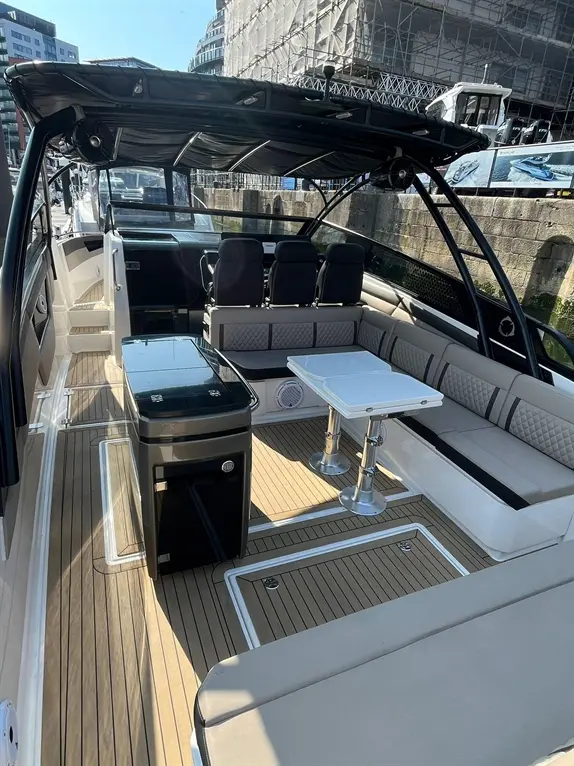 Luxury motorboat interior with plush seating, a small table, and a kitchenette, set in a sunny harbor environment.